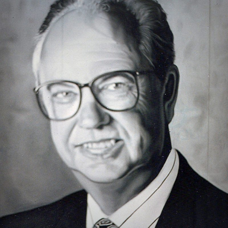 A man in glasses and suit is smiling.