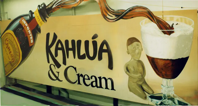 A sign for kahlua and cream with an image of a person sitting on the ground.